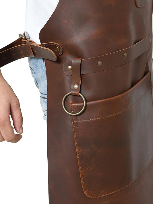 Close-up of brown leather apron side pocket, brass tool ring, rivets, and adjustable waist strap