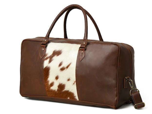 A brown leather duffel bag with a central vertical panel made of brown and white cowhide, featuring two top handles and a detachable shoulder strap, shown on a white background.