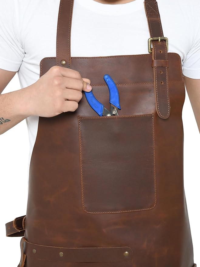 Brown full-grain leather apron chest pocket holding blue pliers beside an adjustable brass-buckle strap