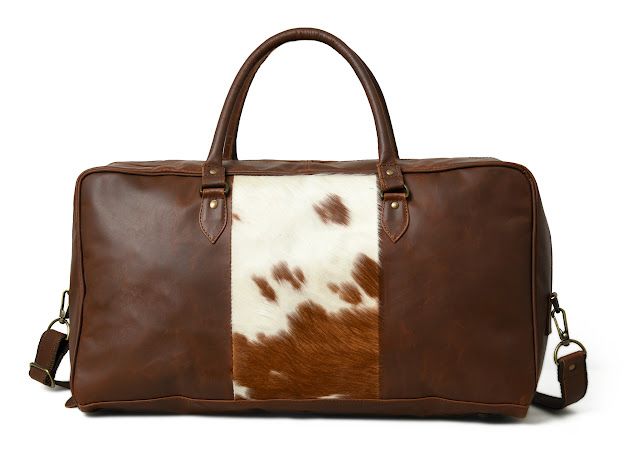 A brown leather duffel bag with a central brown and white cowhide panel, featuring dual top handles and a detachable shoulder strap, shown against a plain white background.