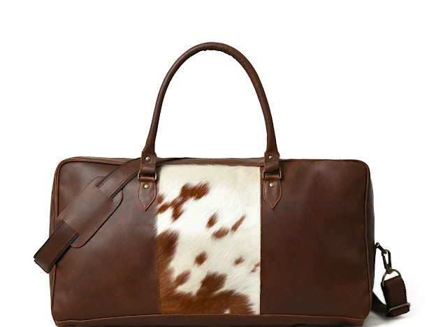 A brown leather duffel bag with a brown and white cowhide panel on the front, featuring two top handles and a detachable shoulder strap, set against a plain white background.